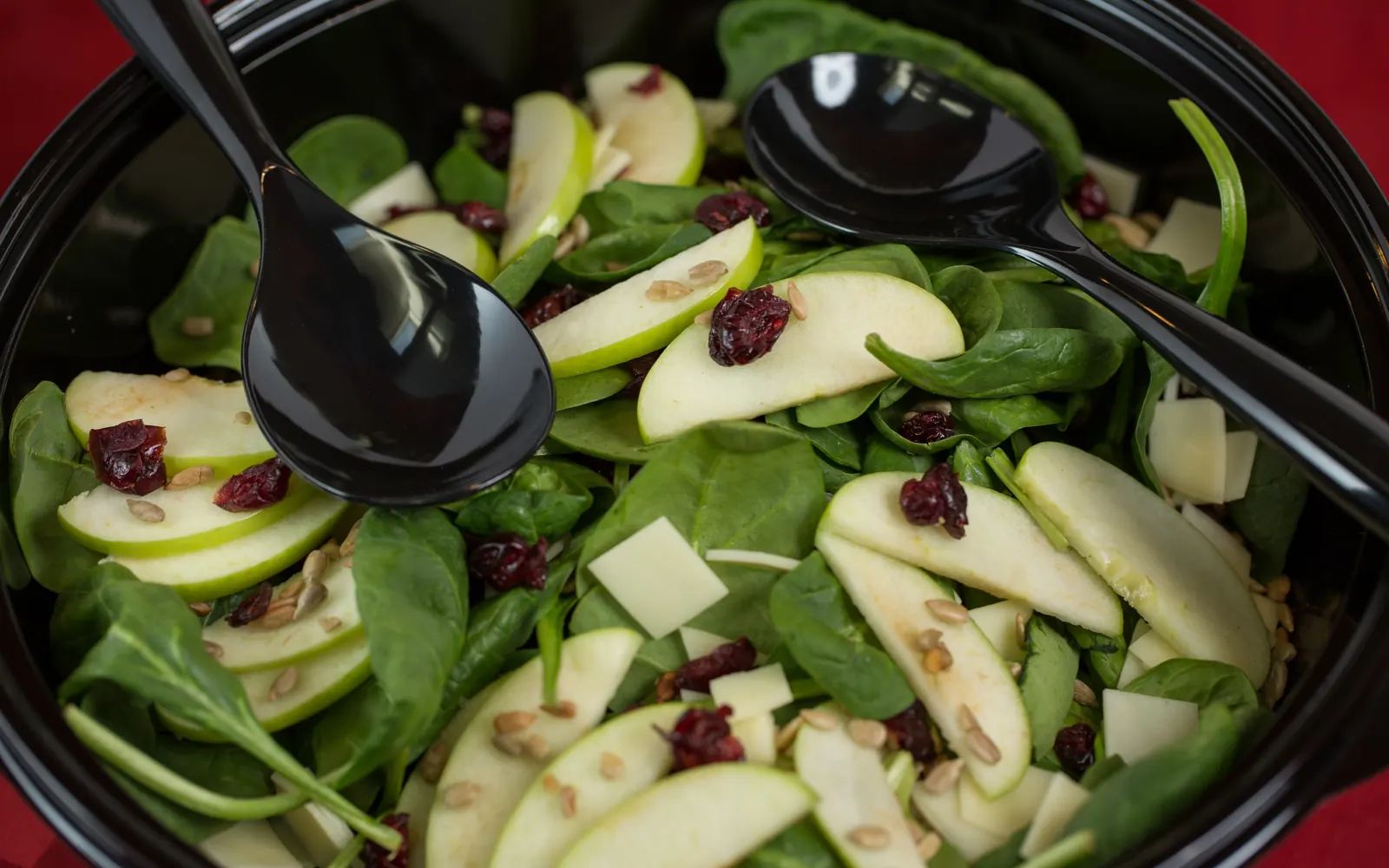 A shareable spinach salad with green apple, cranberries, Swiss and sunflower seeds.