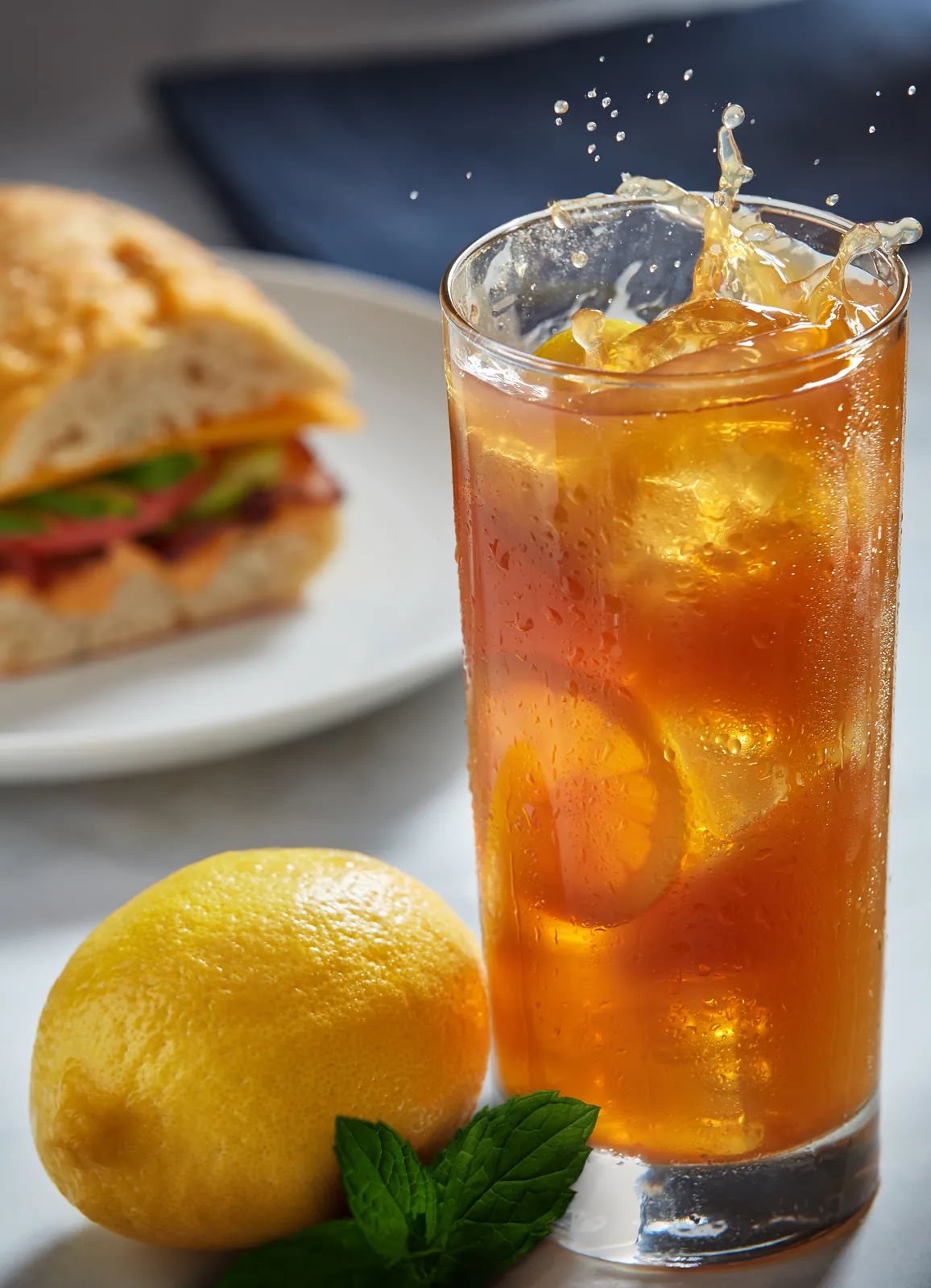 A glass of Islesboro Iced Tea with lemon, beside a lemon and mint.